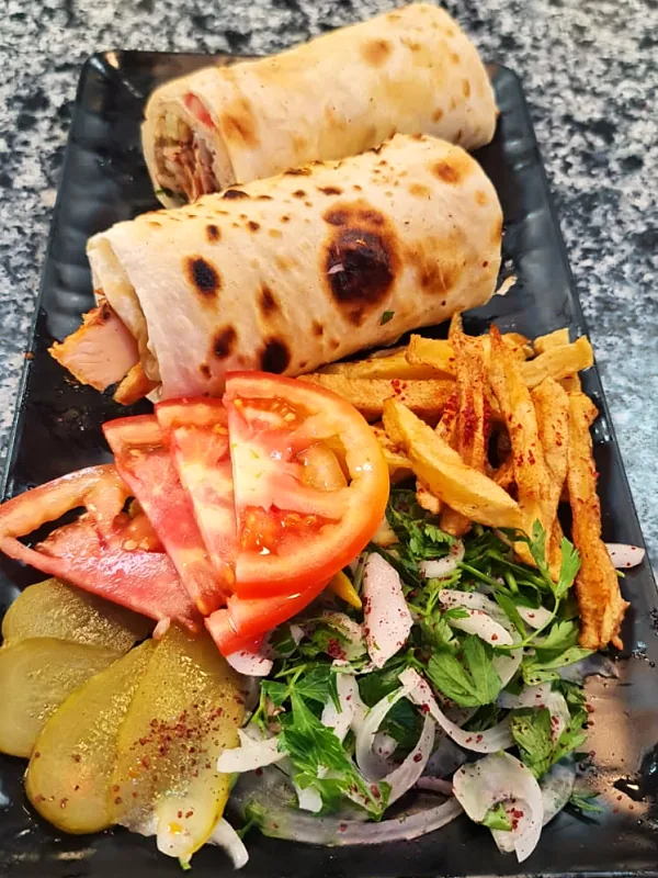 Tabakta ikiye bölünmüş lavaş döner; yanında domates, patates kızartması, soğan piyazı ve turşu
